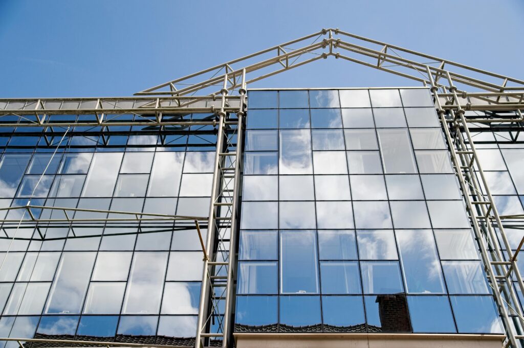 Contemporary glass facade reflecting clouds under a clear blue sky, showcasing modern architecture.